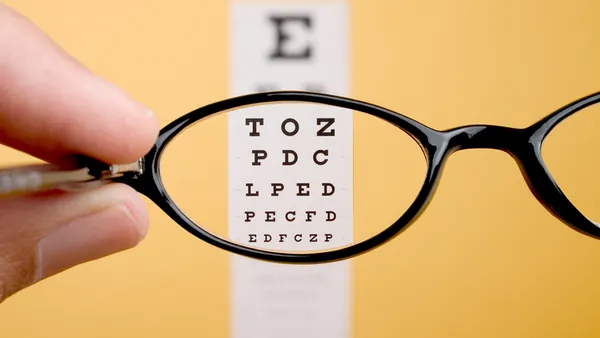 Letters appear clearer in an eye chart on a yellow wall viewed through glasses.