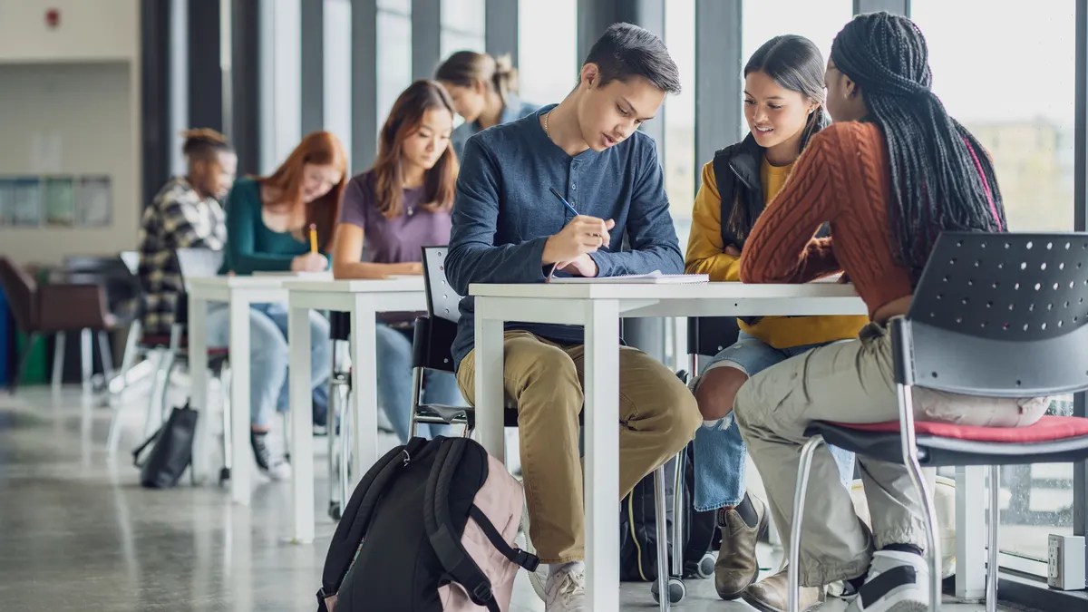 University students are seen scattered at various desks in an open study area, as they work away on assignments between classes.