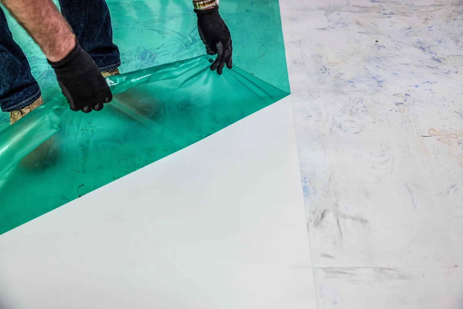 A person removes a green film from a white surface.