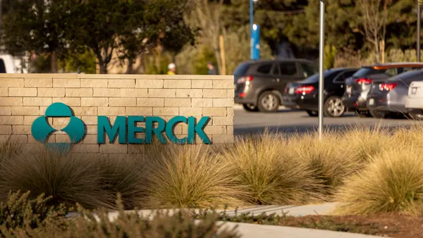 A low stone wall partially obscured by long grass bears a Merck & Co. logo