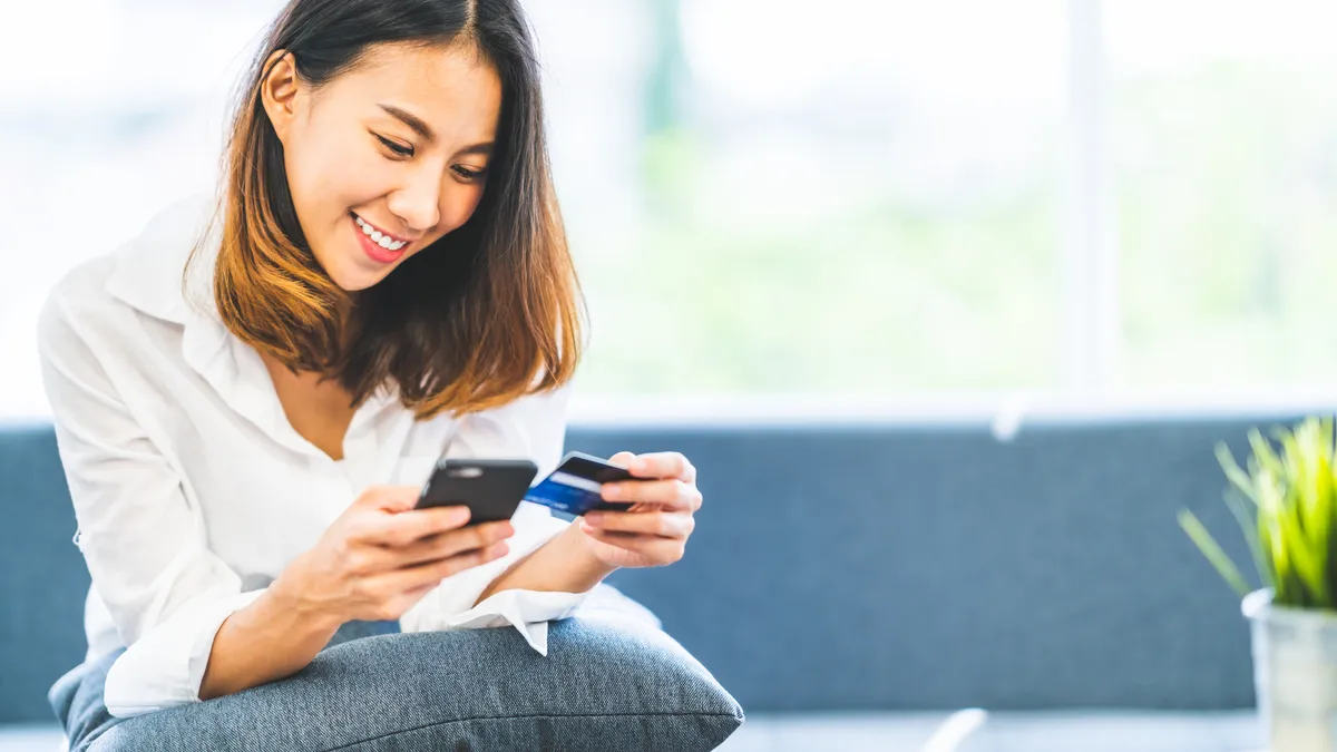 A young woman holding a smartphone and a credit card.