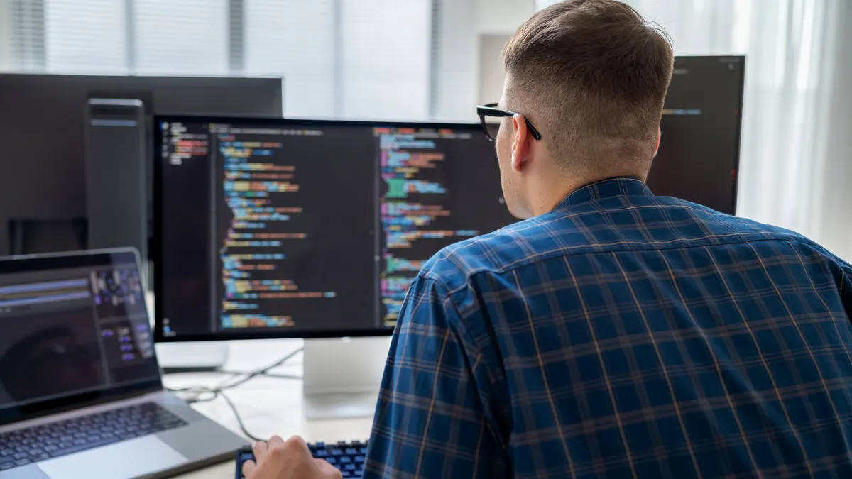 Software developers sit at a desk with multiple screens, using AI agent.