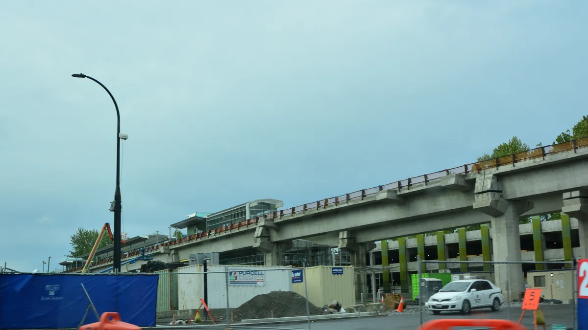 Street view of a train station construction site, with fencing and orange barrels.