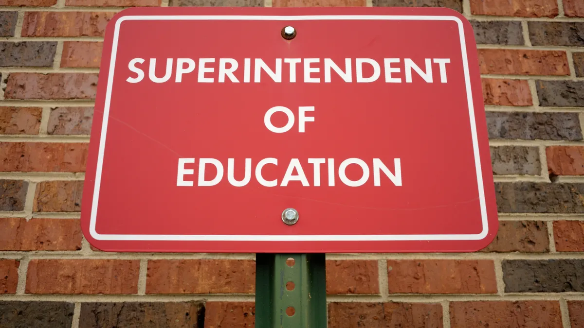 A red sign sits in front of a brick wall. The sign says "superintendent of education"