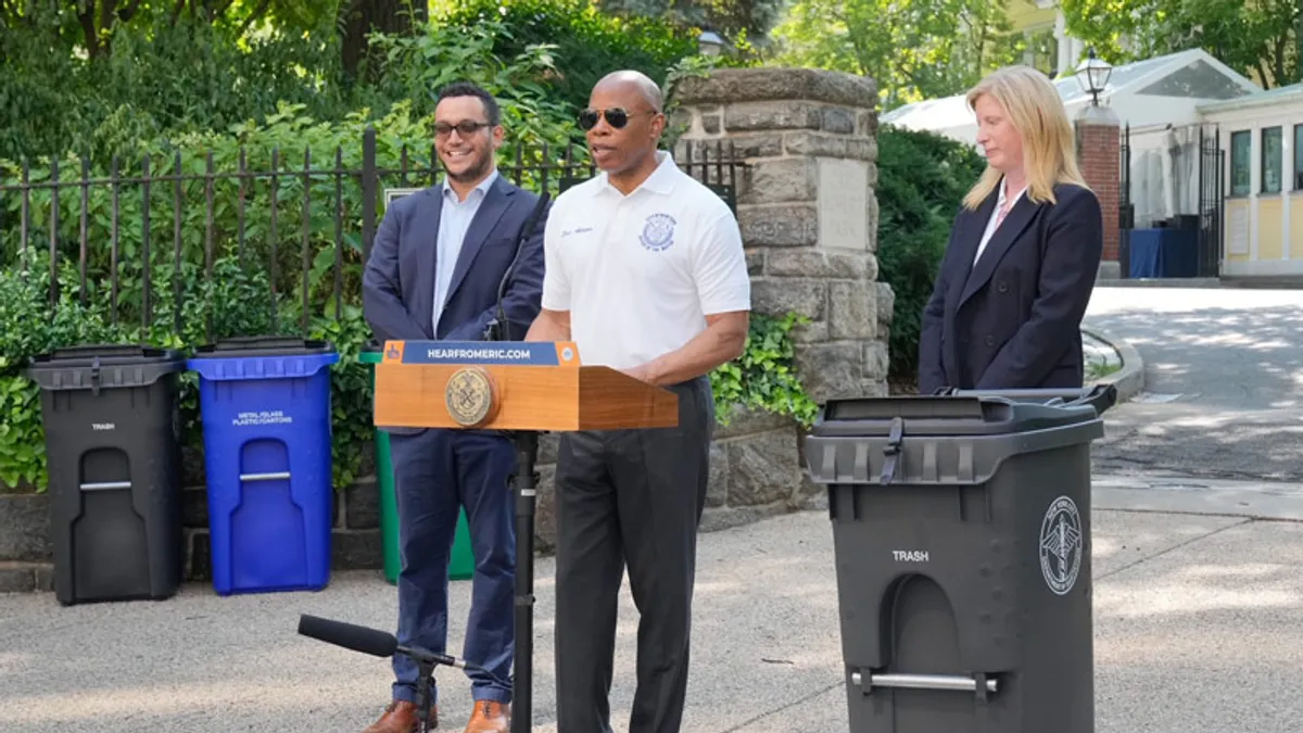 Mayor Eric Adams stands with two officials next to a NYC Bin in front of Gracie Mansion in New York.