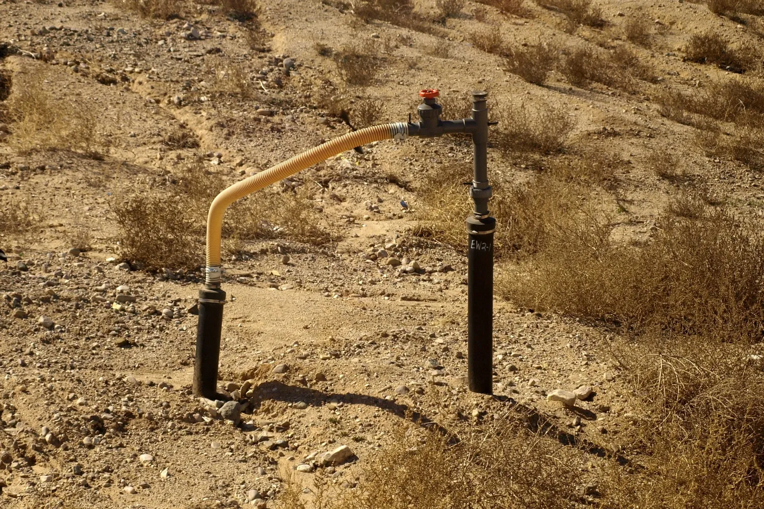 Two small pipes connected by a flexible tube stick out of rocky soil.