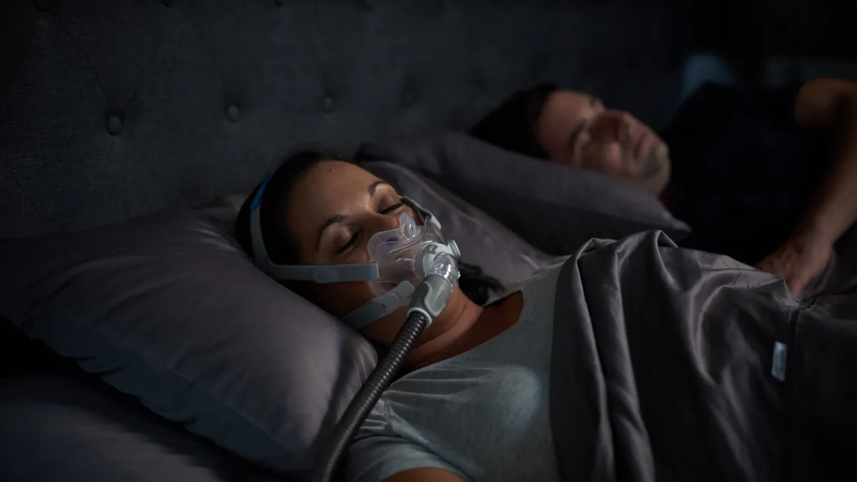 A person lies in bed wearing a CPAP mask over their nose and mouth.