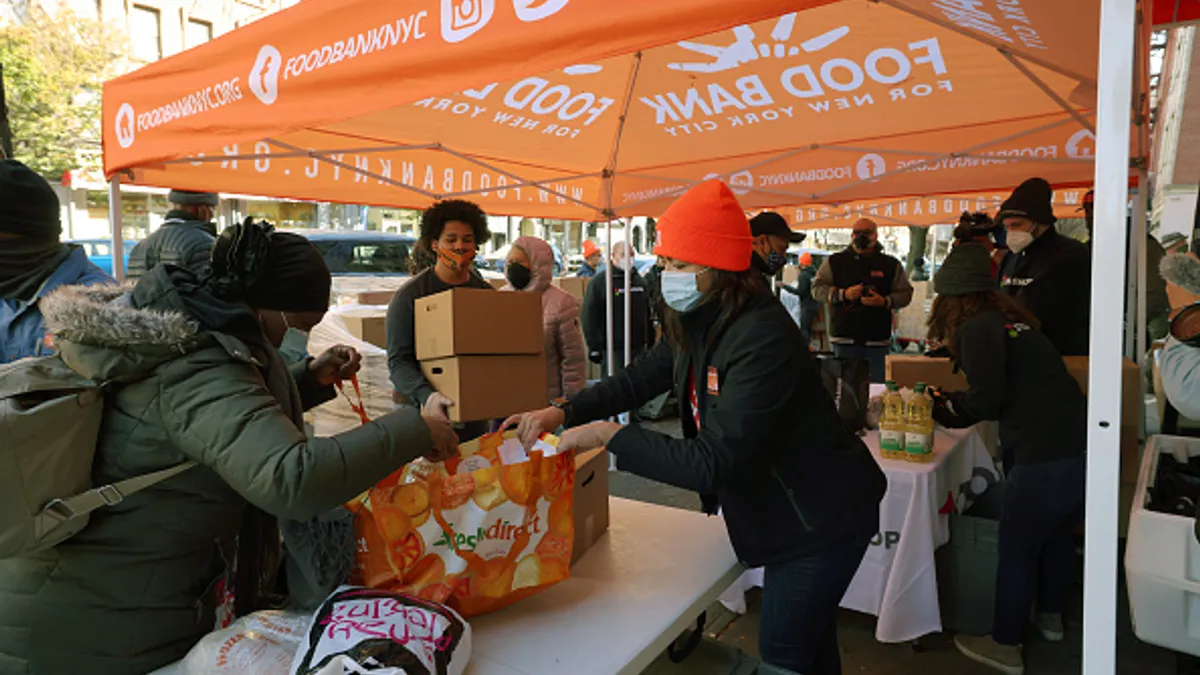 People standing under a tent hand out food in bags and boxes.