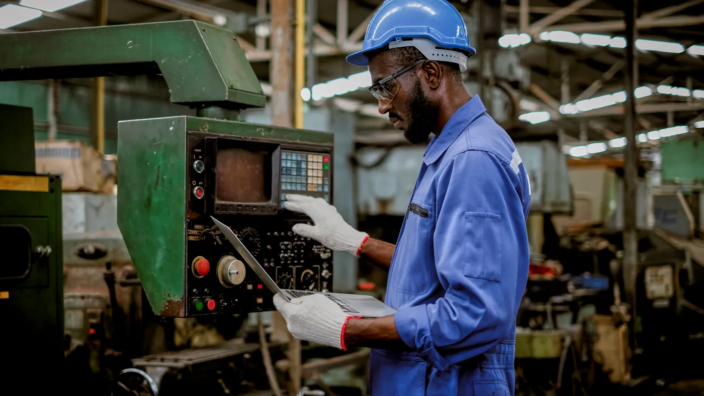 Factory worker in using laptop and push buttons to test the machine