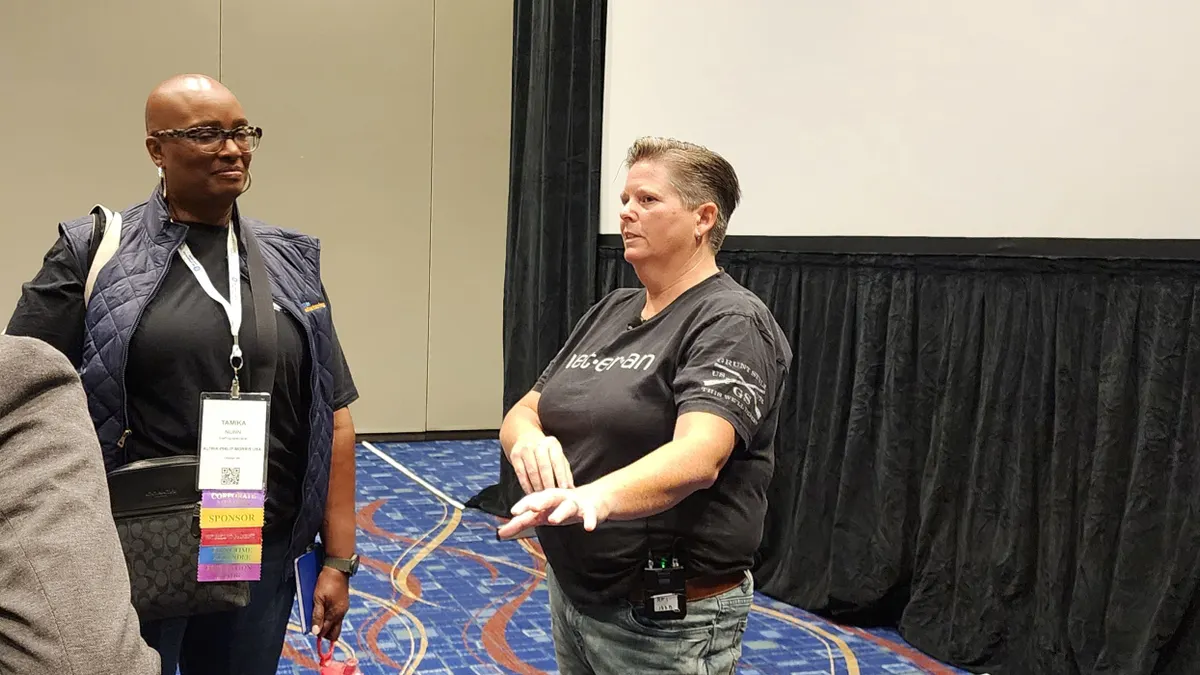 A person with short hair and a black shirt speaking to two people.