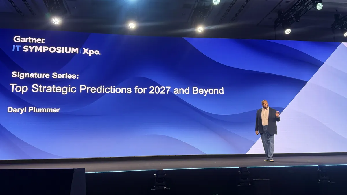 Daryl Plummer, distinguished vice president analyst at Gartner, presented Gartner's top strategic predictions for 2027 in front of a blue slide at Gartner's IT Symposium.