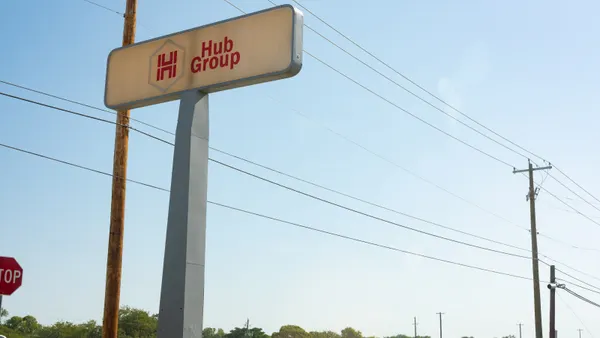 An elevated sign with the Hub Group logo stands against a clear blue sky, with power lines and a stop sign visible nearby.