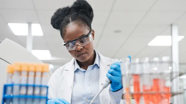 A female scientist fills a well plate with a pipette while working in a laboratory.