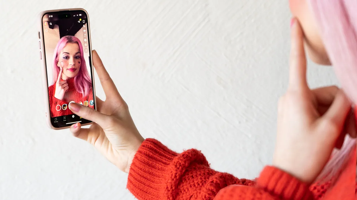 A person holding up a smart phone that shows an image of their face.