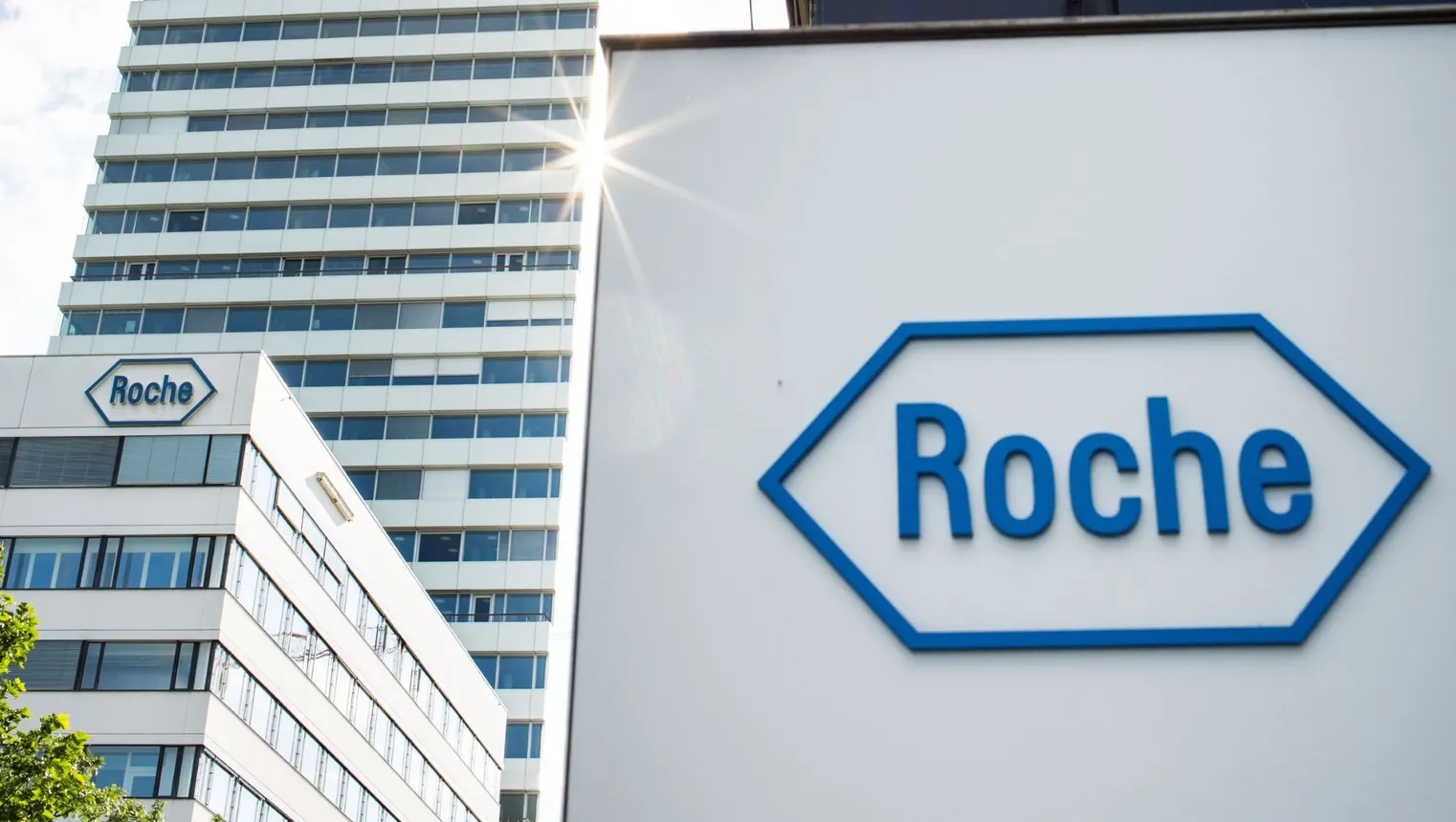 A sign with the Roche logo stands in front of a tall building.