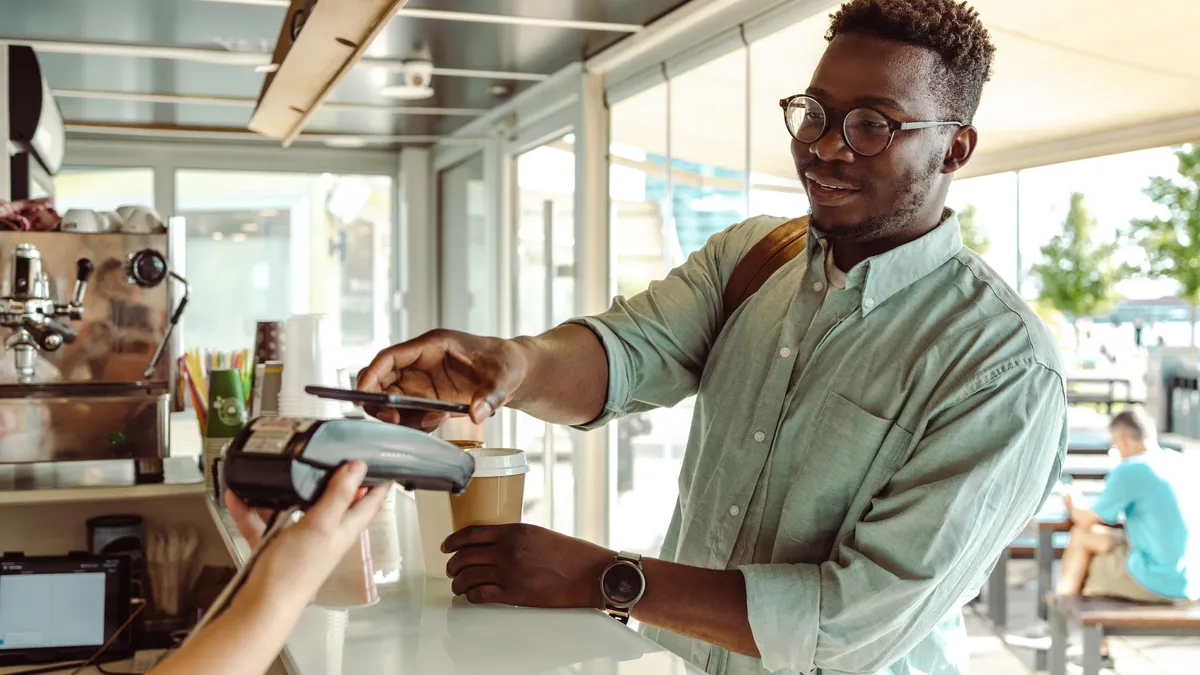 An African American young man paying with a smartphone at a coffee shop