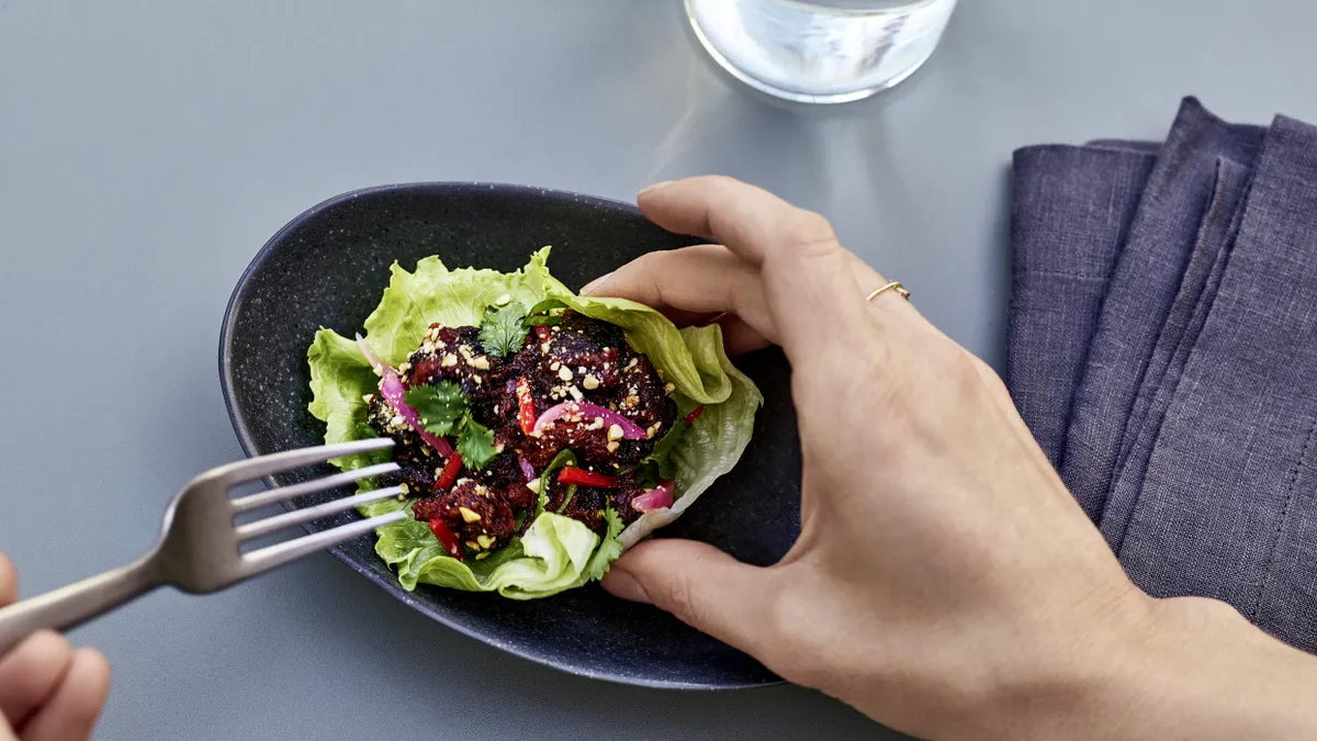 A person uses a fork on a cultivated meat larb salad in a lettuce cup.