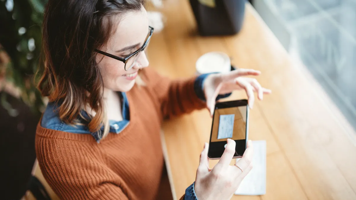 A smiling person takes a picture with their smart phone of a check or paycheck for digital electronic depositing