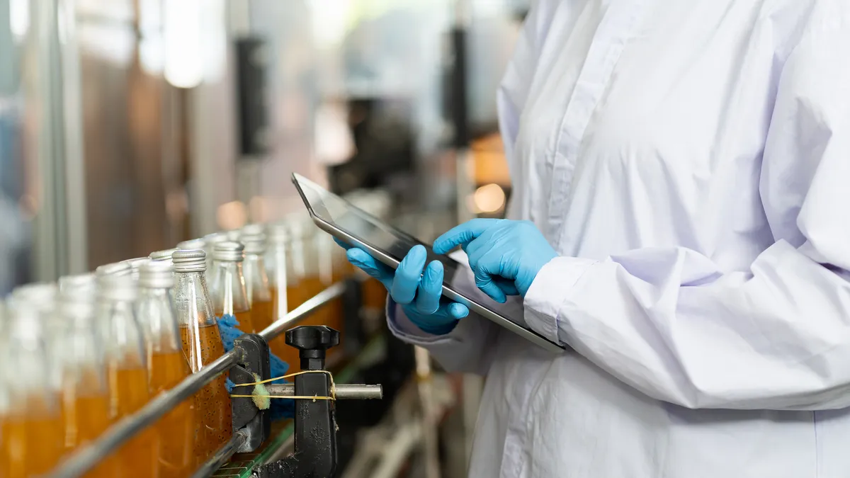 Hands of worker working with digital tablet check product on the conveyor belt in the beverage factory.