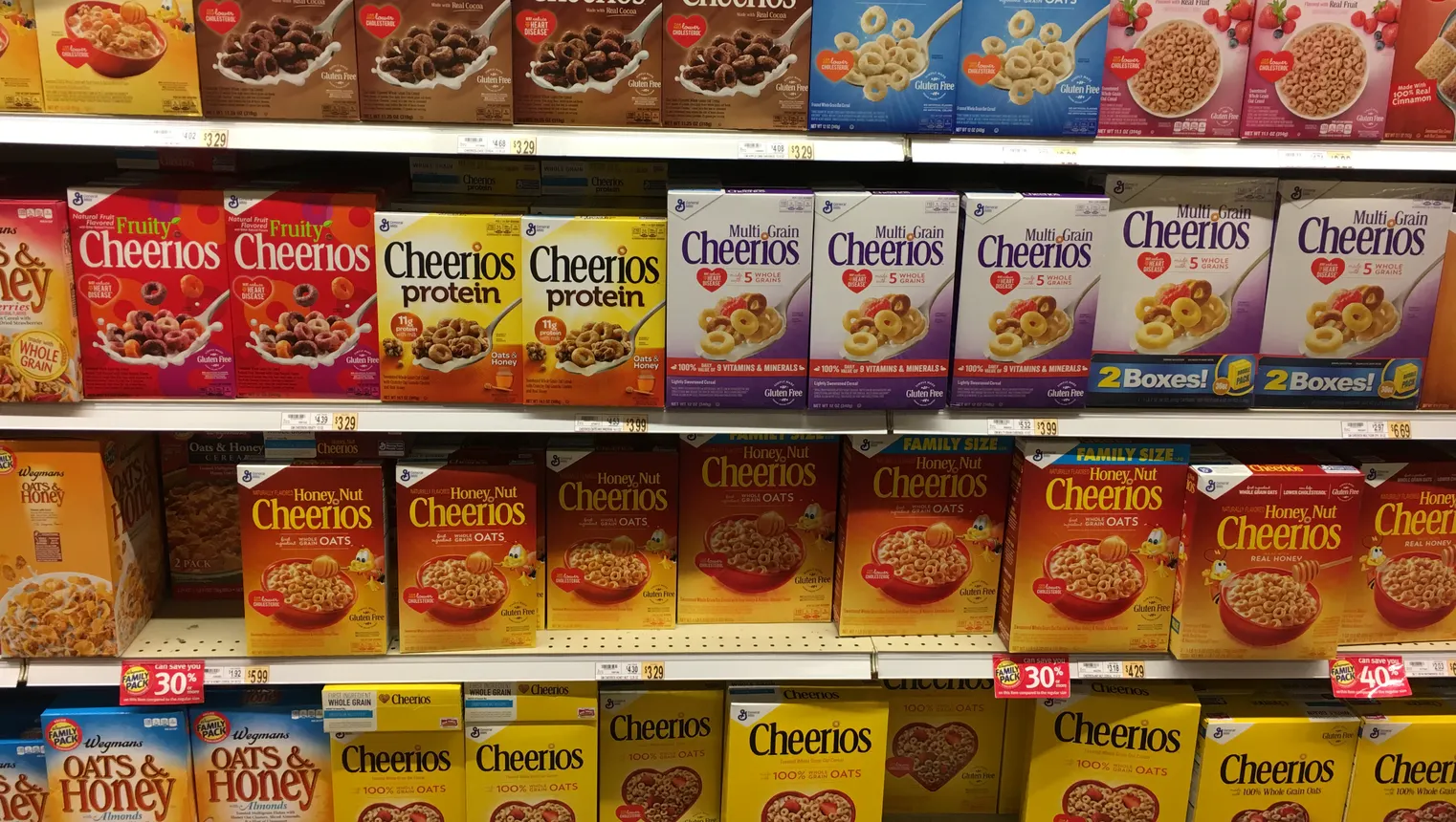 Different varieties of Cheerios on a grocery store shelf.
