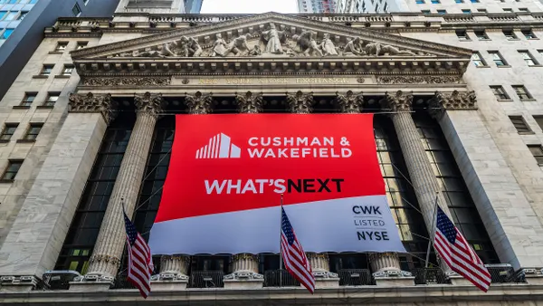 The New York Stock Exchange facade with a large ad that reads "Cushman & Wakefield, What's Next." 