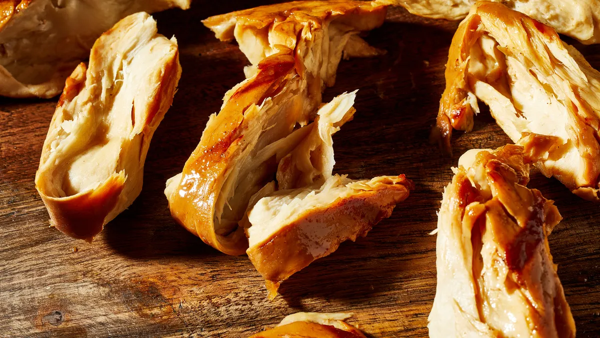 Pieces of roasted and cooked cultivated chicken on a wooden cutting board