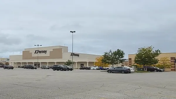 A shopping mall with cars parked in the lot and a few trees.