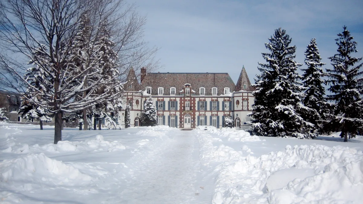 A French-style building sits in the far-ground, behind a snowy lawn and white-capped trees.