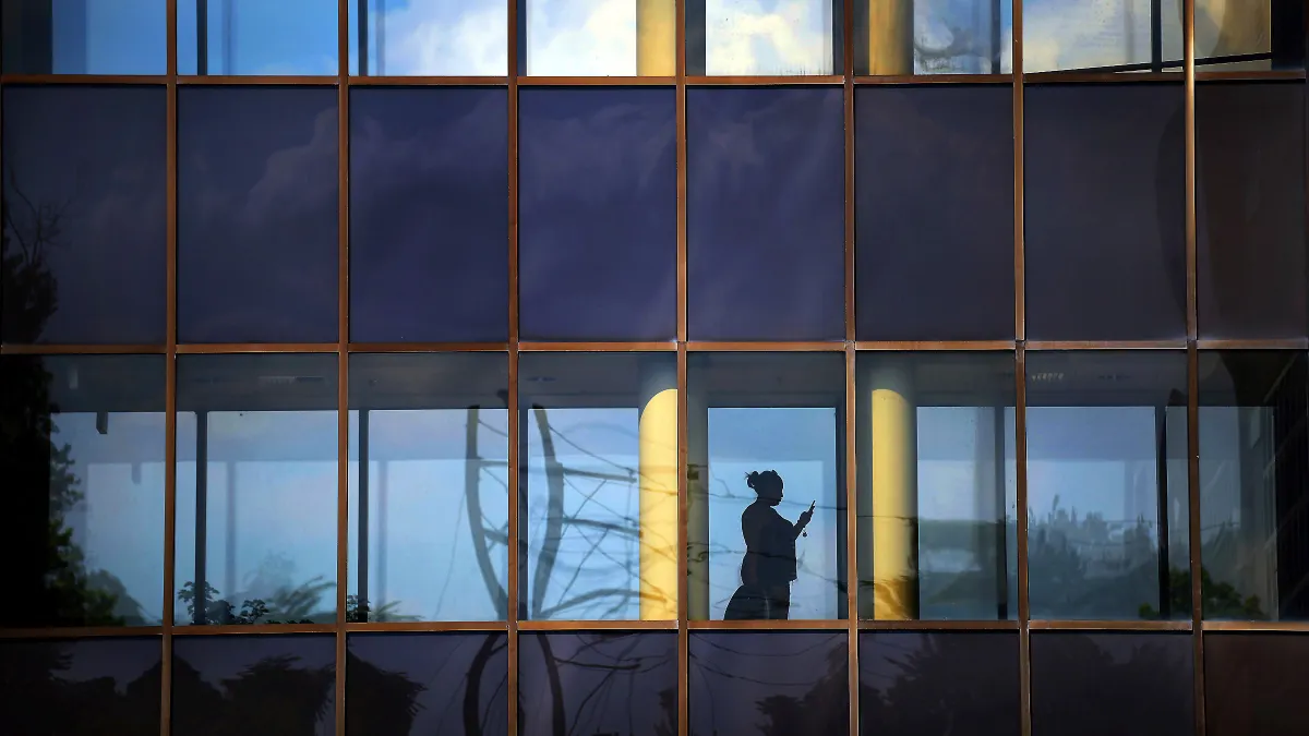 A person stands silhouetted in a window of a glass building facade.