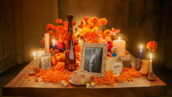 An ofrenda adorned with a picture, Don Julio, flowers, candles and pan de muertos.