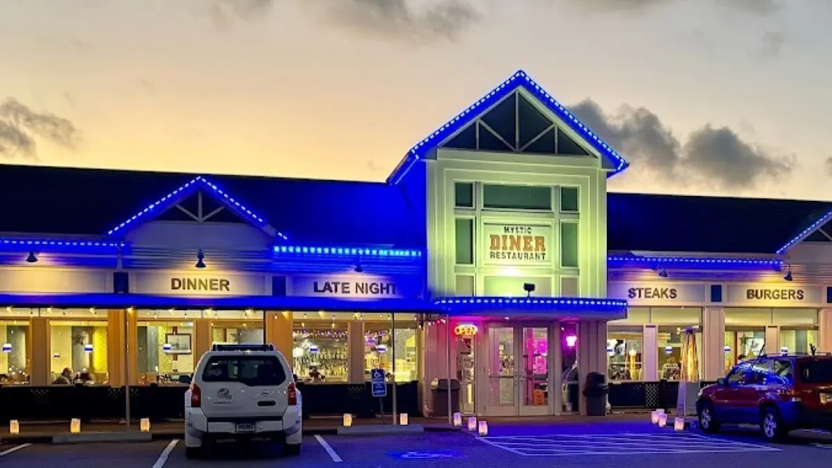 Exterior view of Mystic Diner Restaurant lit up with bright blue lights at sunset.