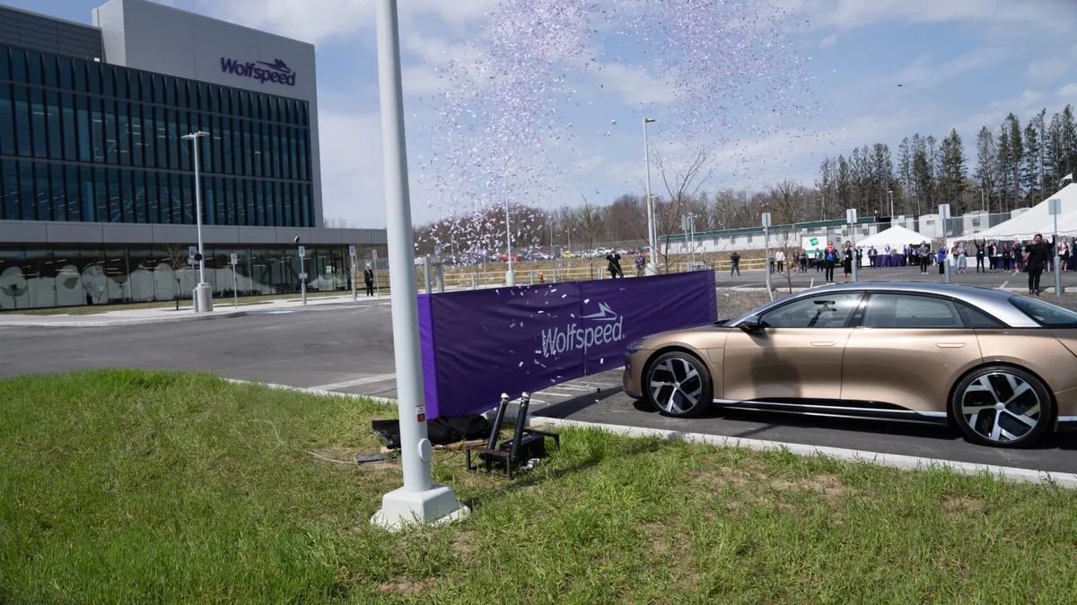 A gold car is about to cut through a purple ribbon with the Wolfspeed logo and  white and purple confetti flying in the air.