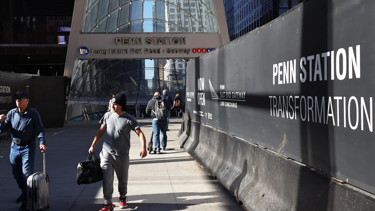 People walk away from the silver and glass Penn Station entrance.