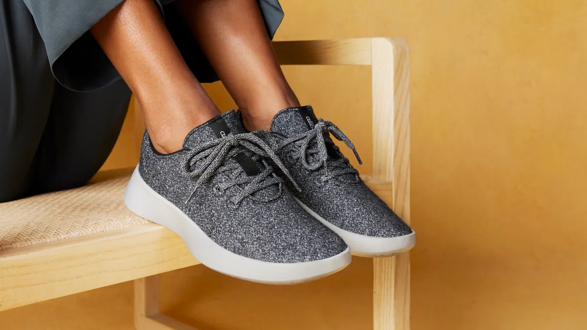 Grey and white Allbirds sneakers modeled on two feet atop a wood chair