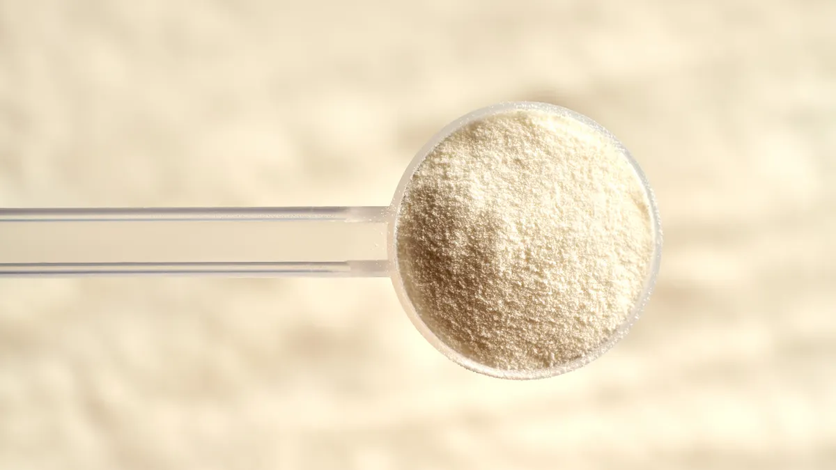 Hands of a person scooping collagen powder from a jar with a scoop.