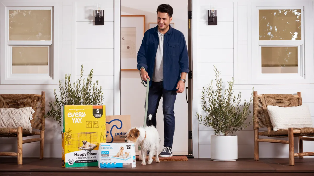 A person walks outside of a home with a dog on a leash and Petco products are on the front porch.