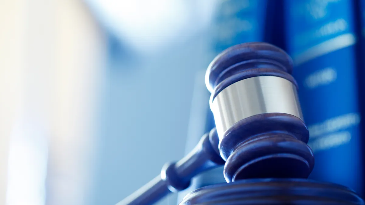 A wooden gavel with metal band rests on a platform. Law books are in the background.