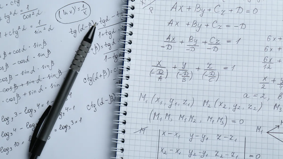 A pen lays on an open notebook of graph paper with a variety of mathematical formulas written on its pages.