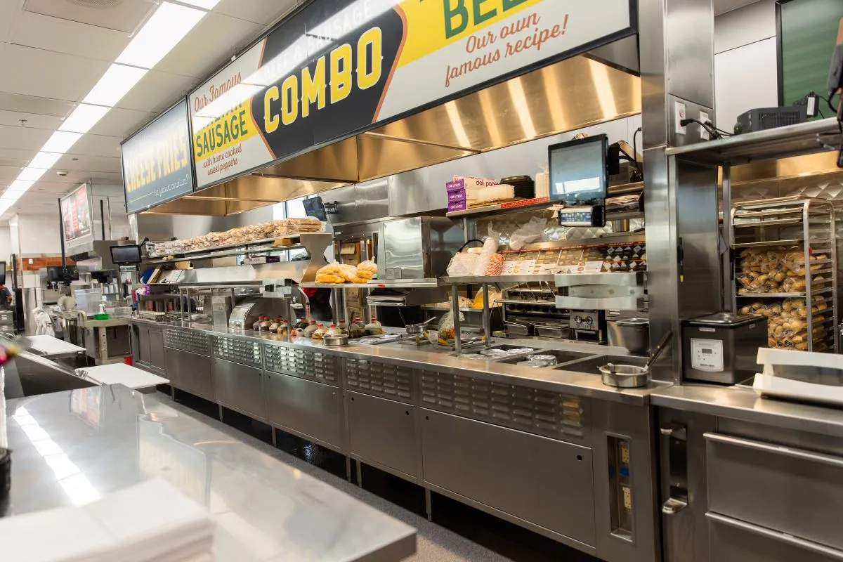 A empty kitchen inside a Portillo's restaurant that includes a makeline and some signage.