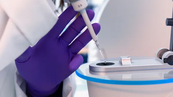 A person uses a syringe to fill a well plate under a microscope.