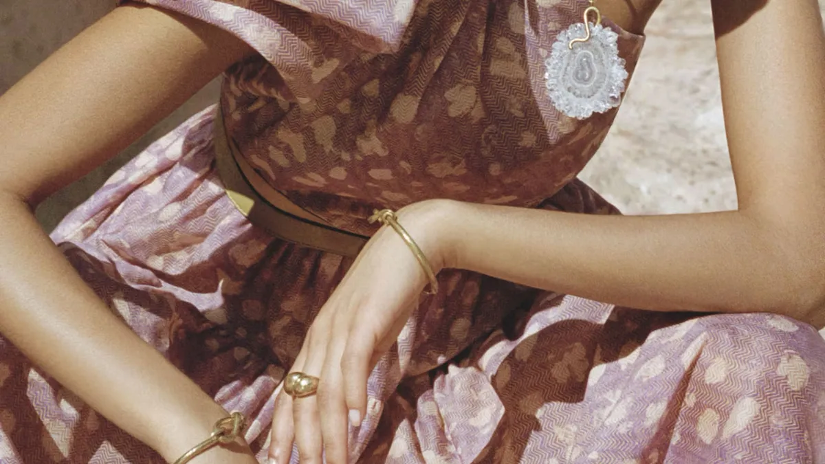 Woman in a brown floral dress sits with her elbows on her knees