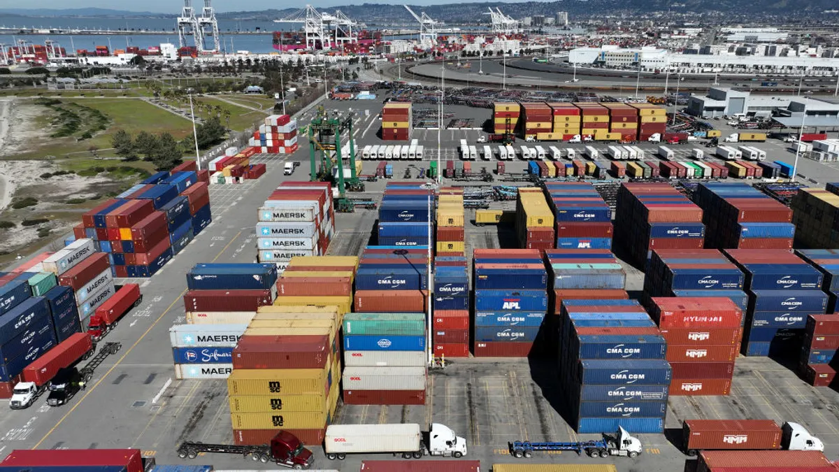 In an aerial view, trucks drive by shipping containers at the Port of Oakland