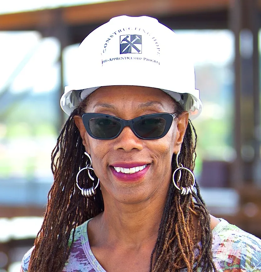 Headshot of a woman in a hard hat and sunglasses.