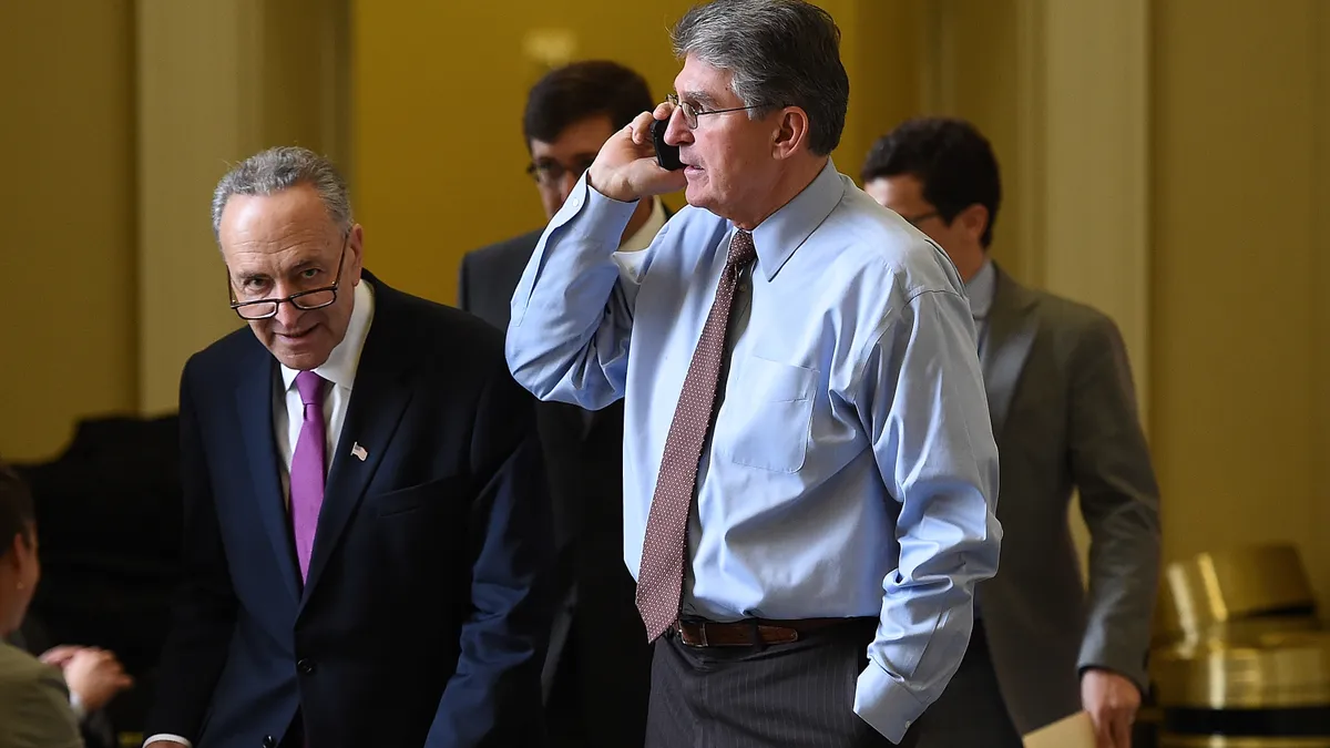 West Virginia Senator Joe Manchin is standing, holding a cell phone with Senate Majority Leader Chuck Schumer alongside.