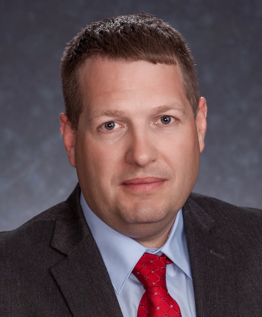 A portrait photo shows a man business executive in a dark suit and red tie.