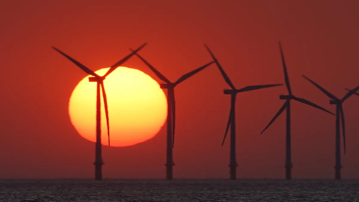 The sun sets behind the wind turbines of Burbo Bank Offshore Wind Farm in the Irish Sea on May 23, 2018 in Wallasey, England.