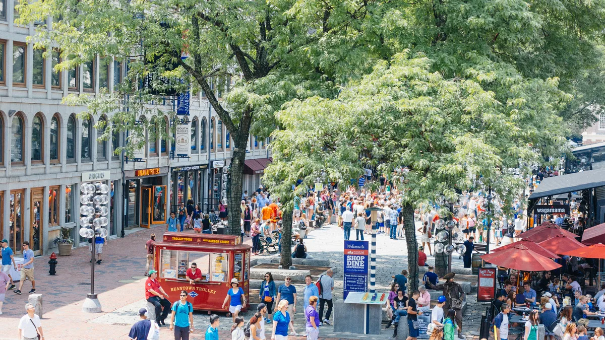 A crowded summer day in a cobblestoned street lined by shops