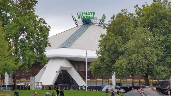 People sit in a gress area in front of a large buildign with a sign on top that reads "Climate Pledge Arena."