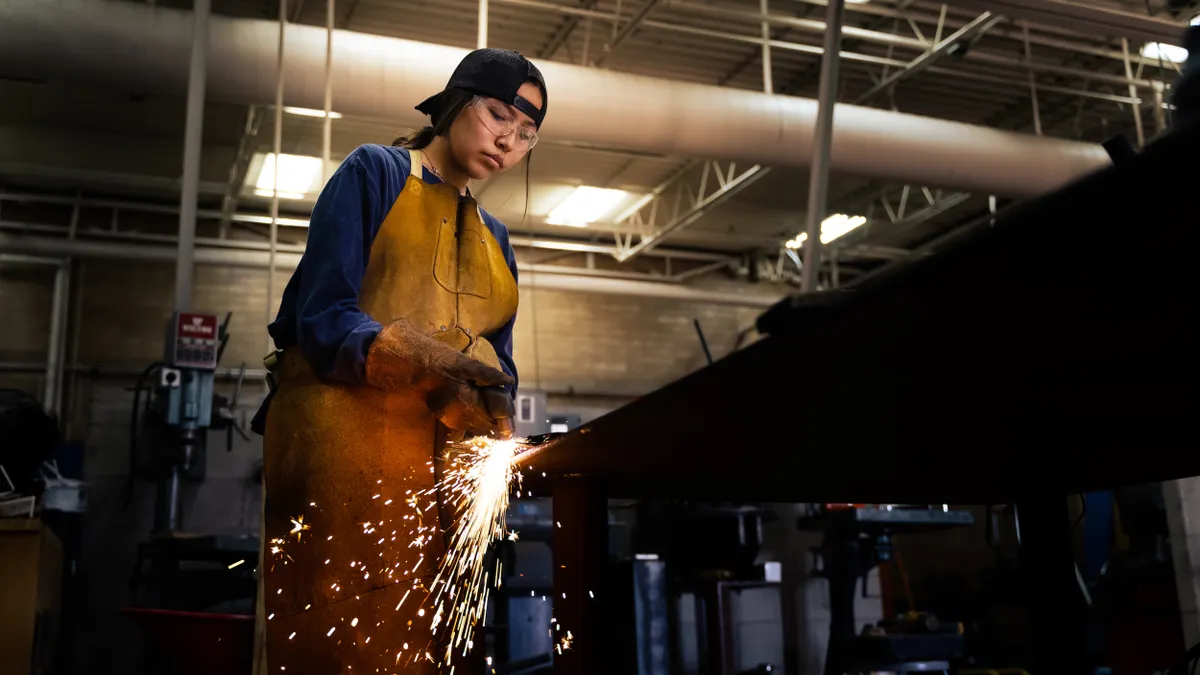 A person uses a torch cutter with a backwards hat in a manufacturing facility