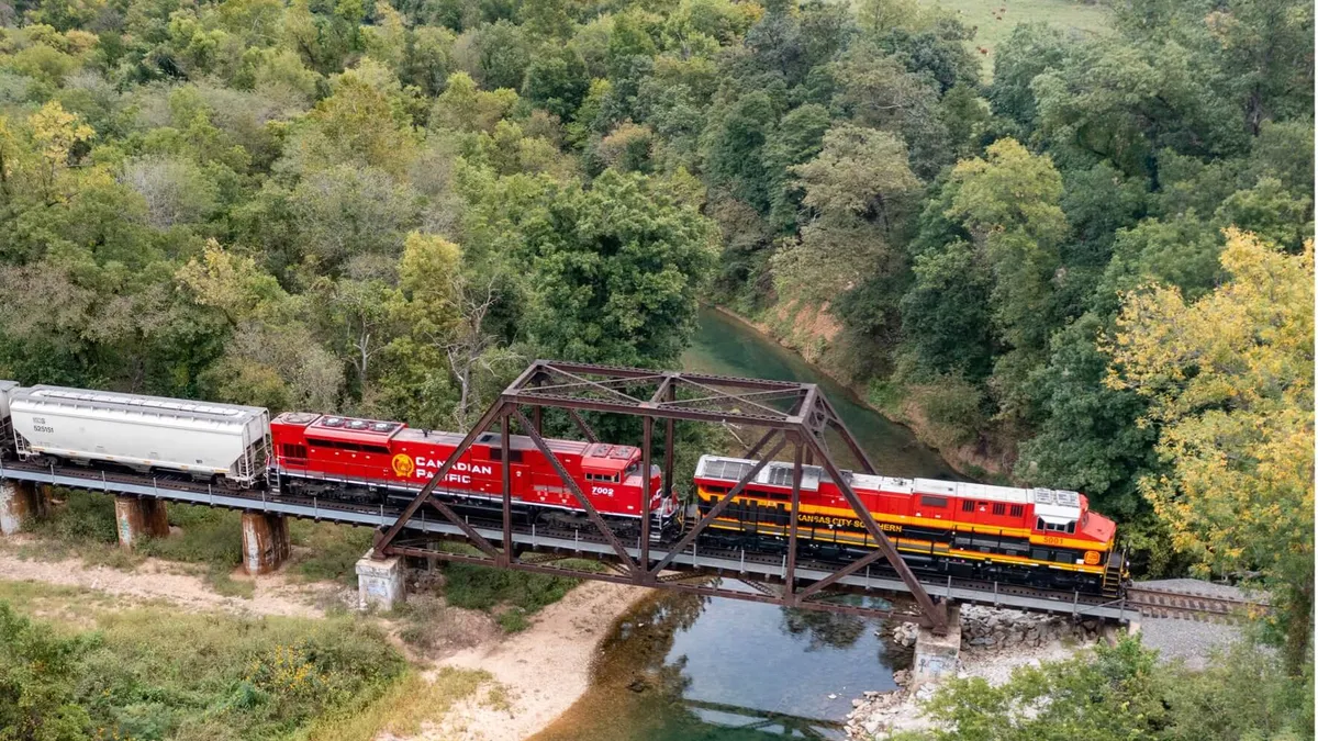 A train crosses a bridge. Two locomotives are seen, one says Canadian Pacific and the other says Kansas City Southern.